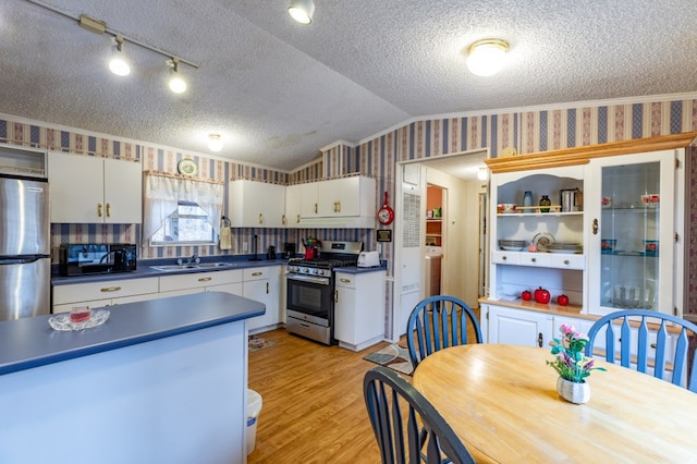 kitchen featuring sink, appliances with stainless steel finishes, white cabinetry, a textured ceiling, and vaulted ceiling