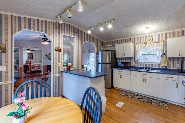 kitchen featuring sink, stainless steel refrigerator, white cabinetry, a textured ceiling, and vaulted ceiling