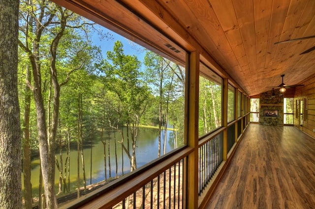 unfurnished sunroom with ceiling fan, lofted ceiling, wooden ceiling, a water view, and an outdoor stone fireplace