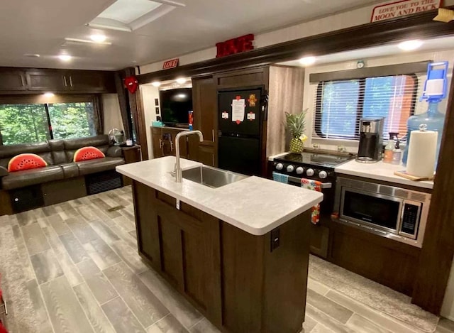 kitchen with dark brown cabinets, black fridge, stainless steel microwave, sink, and a kitchen island with sink