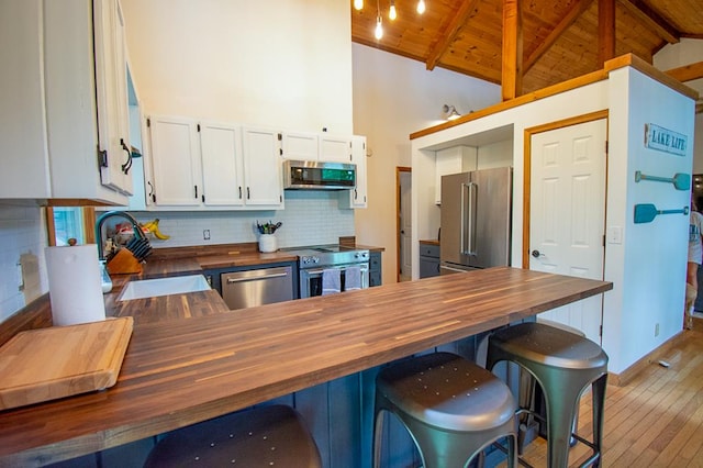 kitchen with butcher block counters, wood ceiling, white cabinets, sink, and appliances with stainless steel finishes