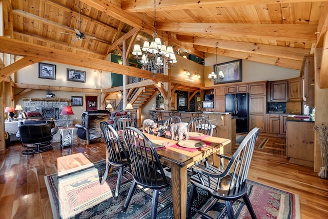 dining area with beam ceiling, a stone fireplace, high vaulted ceiling, hardwood / wood-style floors, and ceiling fan with notable chandelier