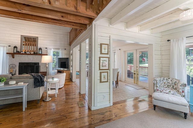 living area featuring wood walls, hardwood / wood-style flooring, beam ceiling, and french doors