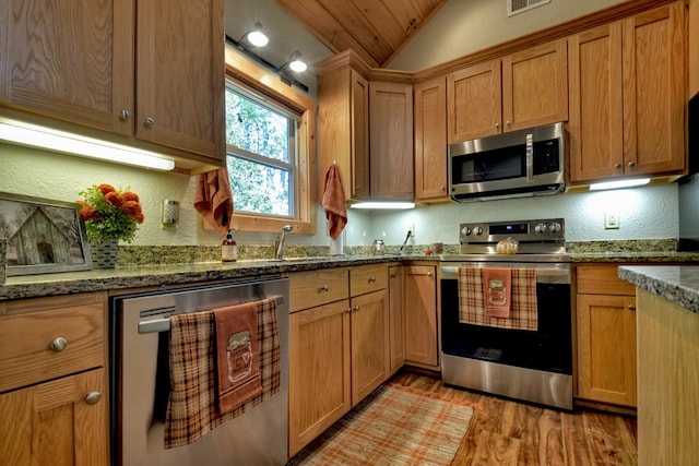 kitchen featuring appliances with stainless steel finishes, lofted ceiling, light wood-type flooring, and dark stone counters