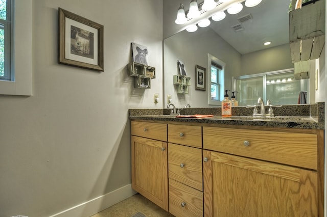 bathroom featuring double vanity, a stall shower, baseboards, visible vents, and a sink