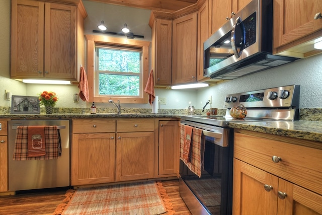 kitchen featuring light wood finished floors, dark stone counters, a textured wall, appliances with stainless steel finishes, and brown cabinets