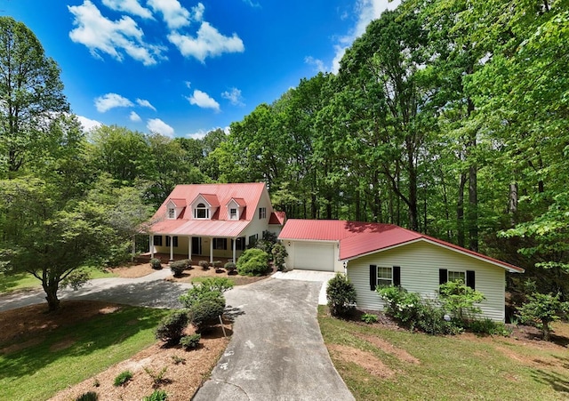 new england style home with a garage, a front lawn, covered porch, metal roof, and driveway