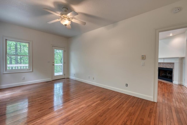 empty room with light wood-style floors, baseboards, ceiling fan, and a fireplace