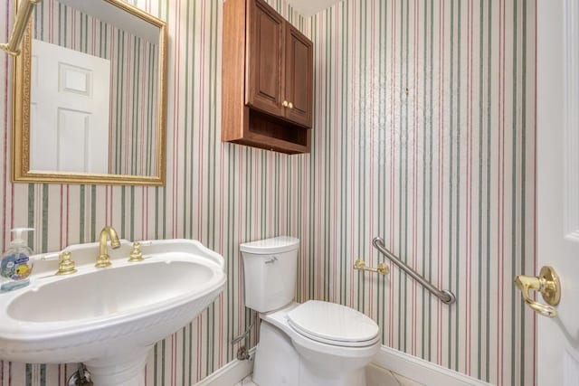 half bath with a sink, baseboards, tile patterned floors, and toilet