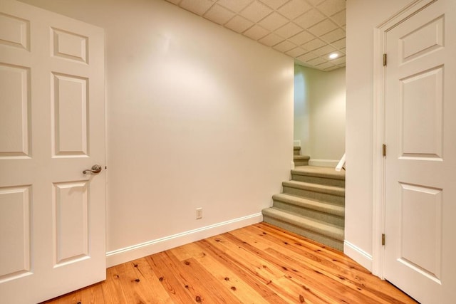 empty room featuring a paneled ceiling, stairs, recessed lighting, baseboards, and wood finished floors