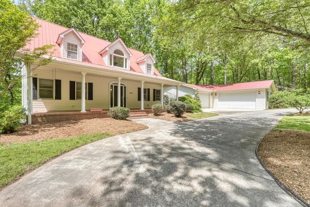 new england style home with a garage, concrete driveway, a porch, and metal roof