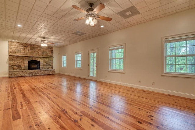 unfurnished living room with baseboards, a ceiling fan, light wood-type flooring, and a stone fireplace
