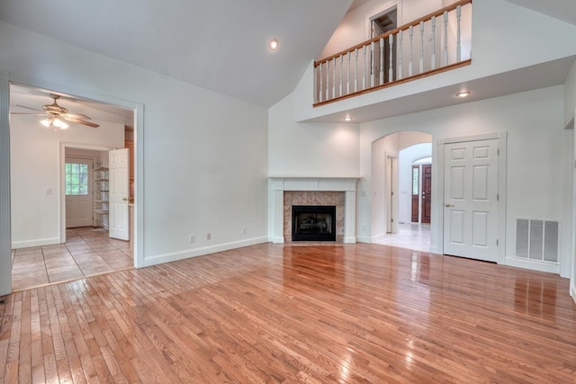 unfurnished living room with ceiling fan, visible vents, arched walkways, high vaulted ceiling, and hardwood / wood-style floors