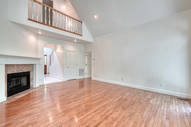 unfurnished living room featuring visible vents, arched walkways, hardwood / wood-style flooring, high vaulted ceiling, and baseboards