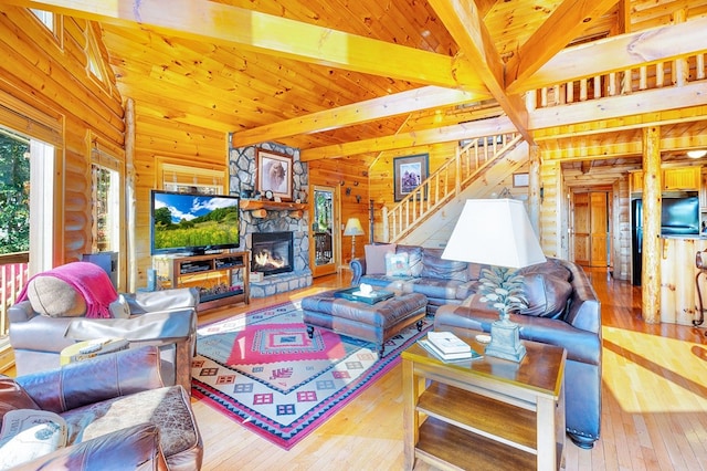 living room with wooden walls, hardwood / wood-style flooring, beam ceiling, a fireplace, and a high ceiling