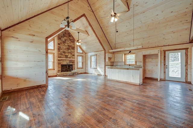 unfurnished living room featuring a healthy amount of sunlight, dark wood-type flooring, a stone fireplace, and wood ceiling