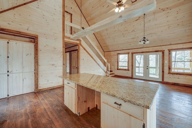 kitchen featuring wooden walls, dark wood-type flooring, light stone countertops, decorative light fixtures, and a center island