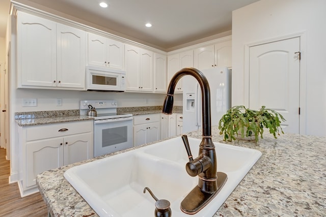 kitchen featuring sink, light stone counters, light hardwood / wood-style flooring, white appliances, and white cabinets