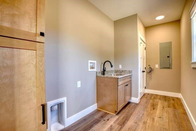 interior space with cabinets, hookup for a washing machine, light hardwood / wood-style floors, sink, and electric panel