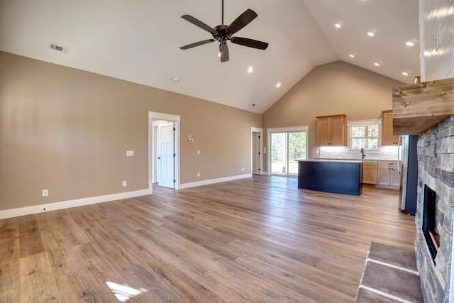 unfurnished living room with a stone fireplace, ceiling fan, high vaulted ceiling, and light wood-type flooring