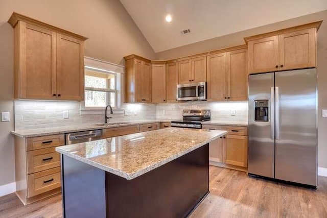 kitchen featuring sink, light hardwood / wood-style flooring, vaulted ceiling, a kitchen island, and appliances with stainless steel finishes