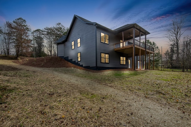 property exterior at dusk featuring a lawn, ceiling fan, a balcony, and a deck