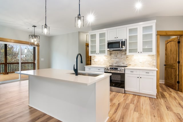 kitchen with appliances with stainless steel finishes, sink, decorative light fixtures, light hardwood / wood-style flooring, and an island with sink