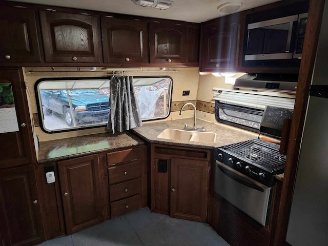 kitchen with gas stove, dark brown cabinetry, a sink, and freestanding refrigerator