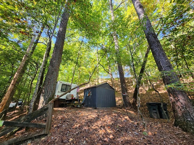 view of yard featuring an outbuilding, a forest view, and a shed