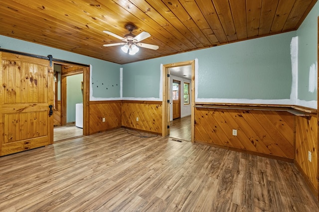 unfurnished room with wooden walls, ceiling fan, wooden ceiling, hardwood / wood-style flooring, and a barn door