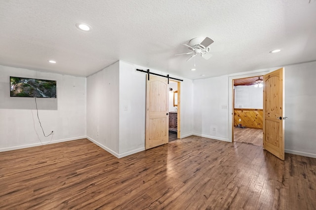 unfurnished bedroom featuring a textured ceiling, hardwood / wood-style floors, connected bathroom, a barn door, and ceiling fan