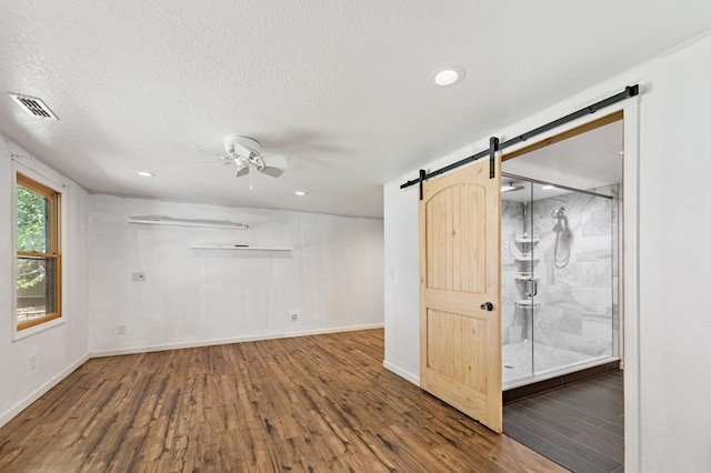 empty room featuring a textured ceiling, wood-type flooring, ceiling fan, and a barn door