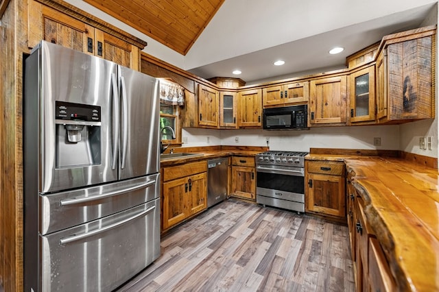 kitchen featuring light wood-type flooring, appliances with stainless steel finishes, sink, lofted ceiling, and butcher block countertops