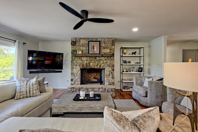living room with crown molding, a ceiling fan, wood finished floors, and a stone fireplace