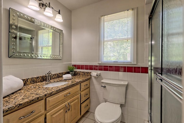 full bath featuring tile walls, vanity, a wainscoted wall, toilet, and a shower with door
