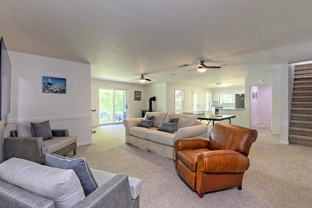 living area with ceiling fan, light carpet, and stairway
