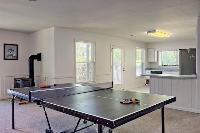 rec room with a sink, a wood stove, wainscoting, and light carpet