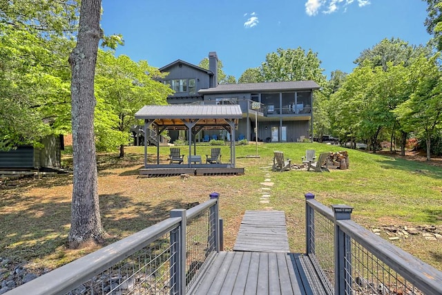 rear view of house with a chimney, a wooden deck, a sunroom, a gazebo, and a yard