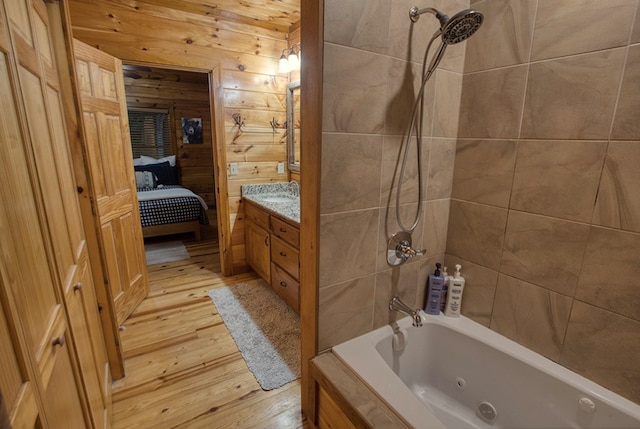 bathroom with wood walls, tiled shower / bath, vanity, and wood-type flooring