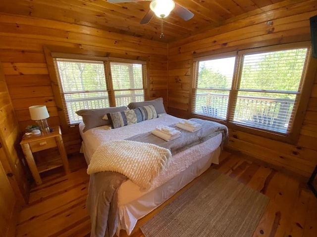 bedroom with multiple windows, wood-type flooring, ceiling fan, and wooden walls