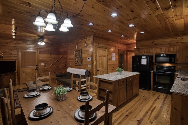 kitchen with wooden walls, light stone counters, ceiling fan, light hardwood / wood-style floors, and black appliances