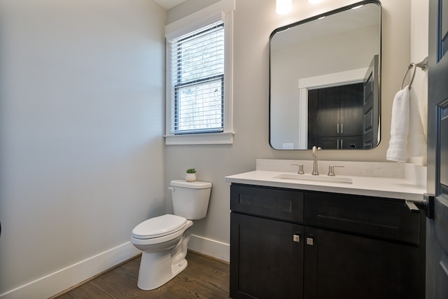 half bath with baseboards, toilet, wood finished floors, and vanity