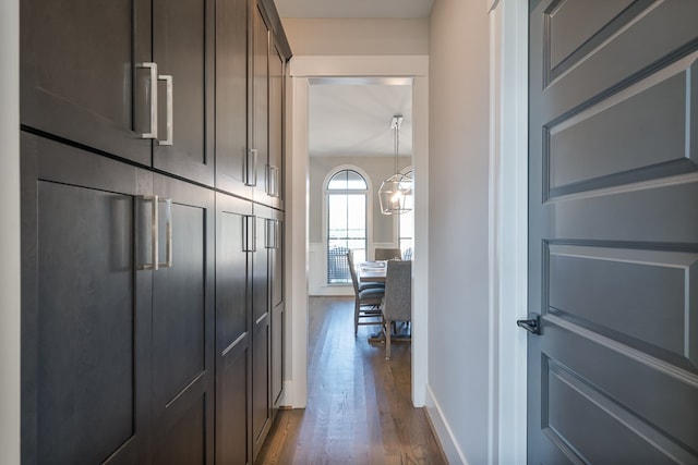 hall featuring dark wood-type flooring, baseboards, and a chandelier