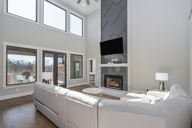 living room with dark wood-type flooring, ceiling fan, a towering ceiling, and a premium fireplace