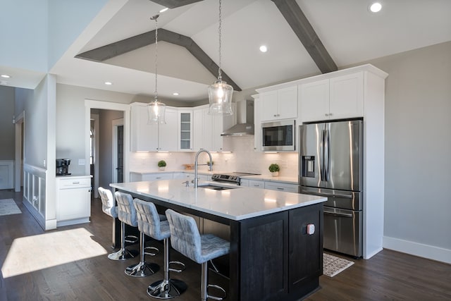 kitchen with dark hardwood / wood-style flooring, wall chimney exhaust hood, appliances with stainless steel finishes, a center island with sink, and white cabinets