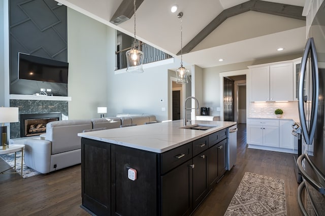 kitchen featuring a fireplace, stainless steel appliances, beamed ceiling, sink, and an island with sink