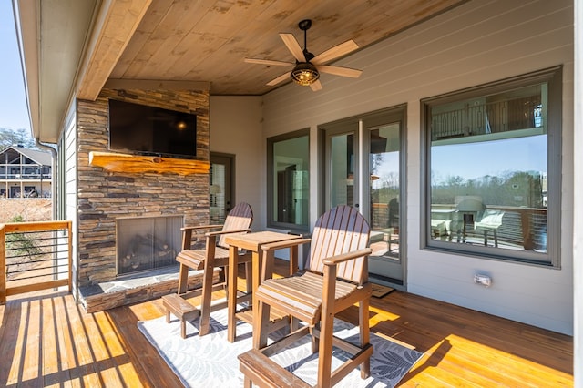 wooden deck featuring a ceiling fan and an outdoor stone fireplace