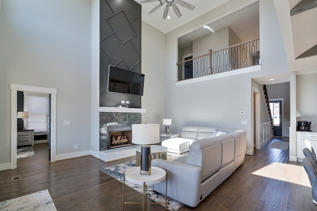 living room with a high end fireplace, a high ceiling, ceiling fan, and dark hardwood / wood-style floors