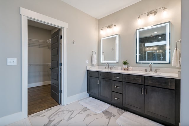 bathroom with double vanity, baseboards, marble finish floor, and a sink