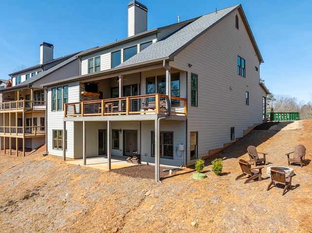 rear view of house featuring a patio, a fire pit, roof with shingles, and a chimney